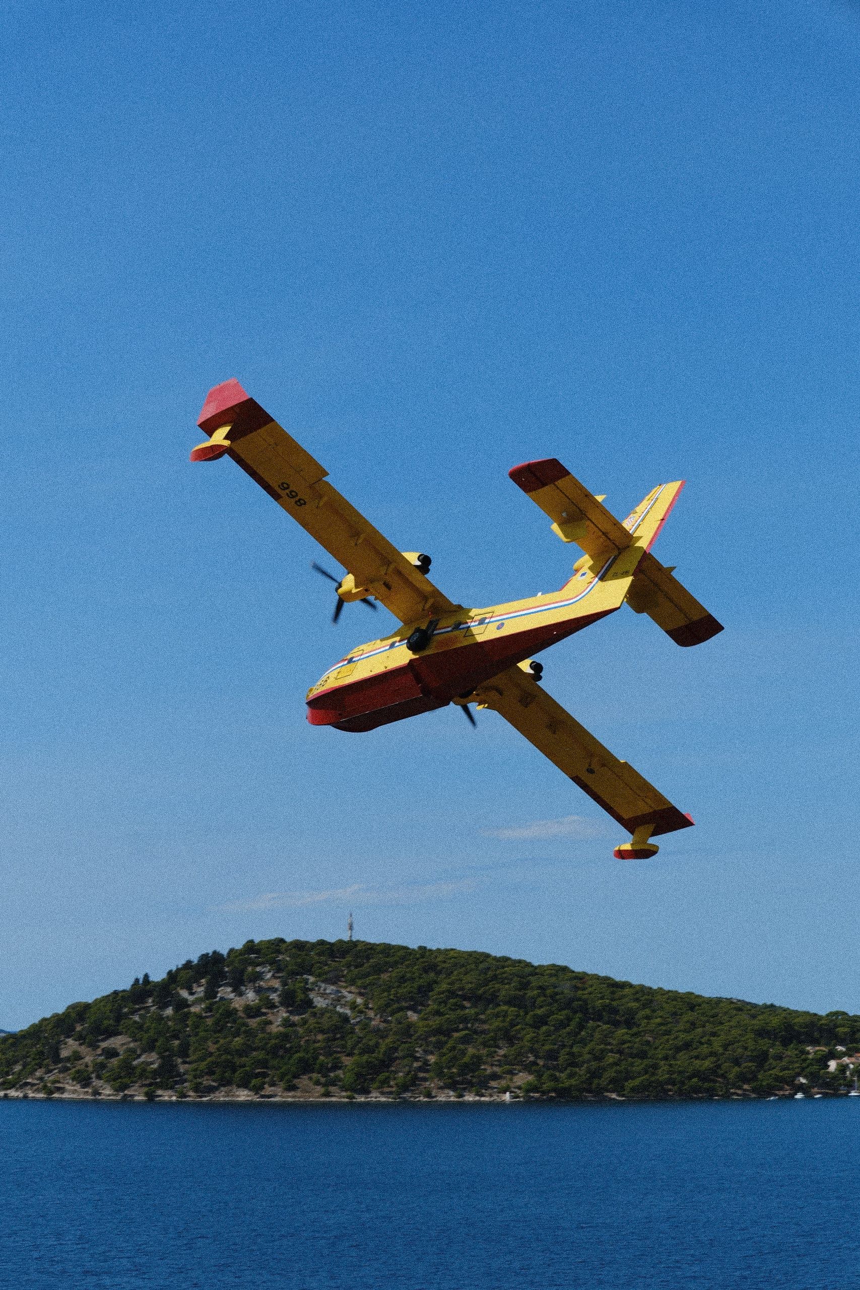 A Canadair banking low over the islands, yellow and red against the Adriatic.